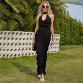 Woman in a black dress standing outdoors with greenery and a stone wall in the background