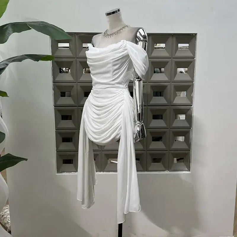 White draped dress on a mannequin with a geometric wall in the background
