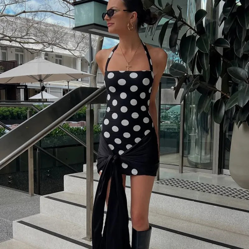 Woman in a black and white polka dot dress standing outdoors near steps and plants.