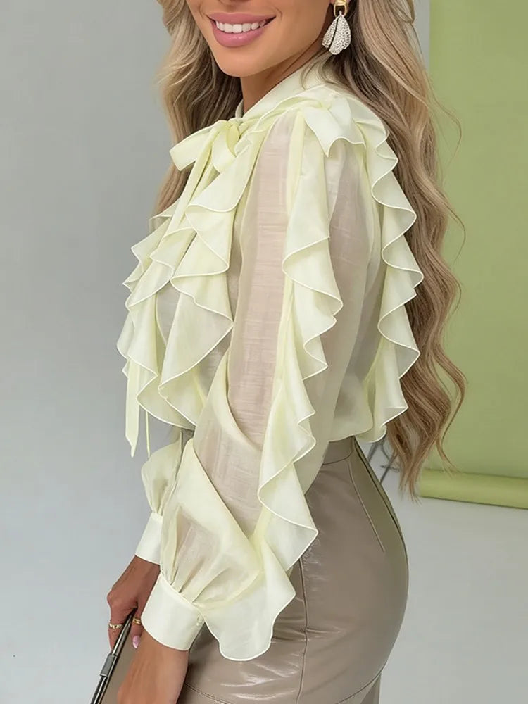 Woman wearing a light green ruffled blouse with a plain background