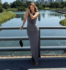 Woman in a gray dress standing by a lake with a city skyline in the background
