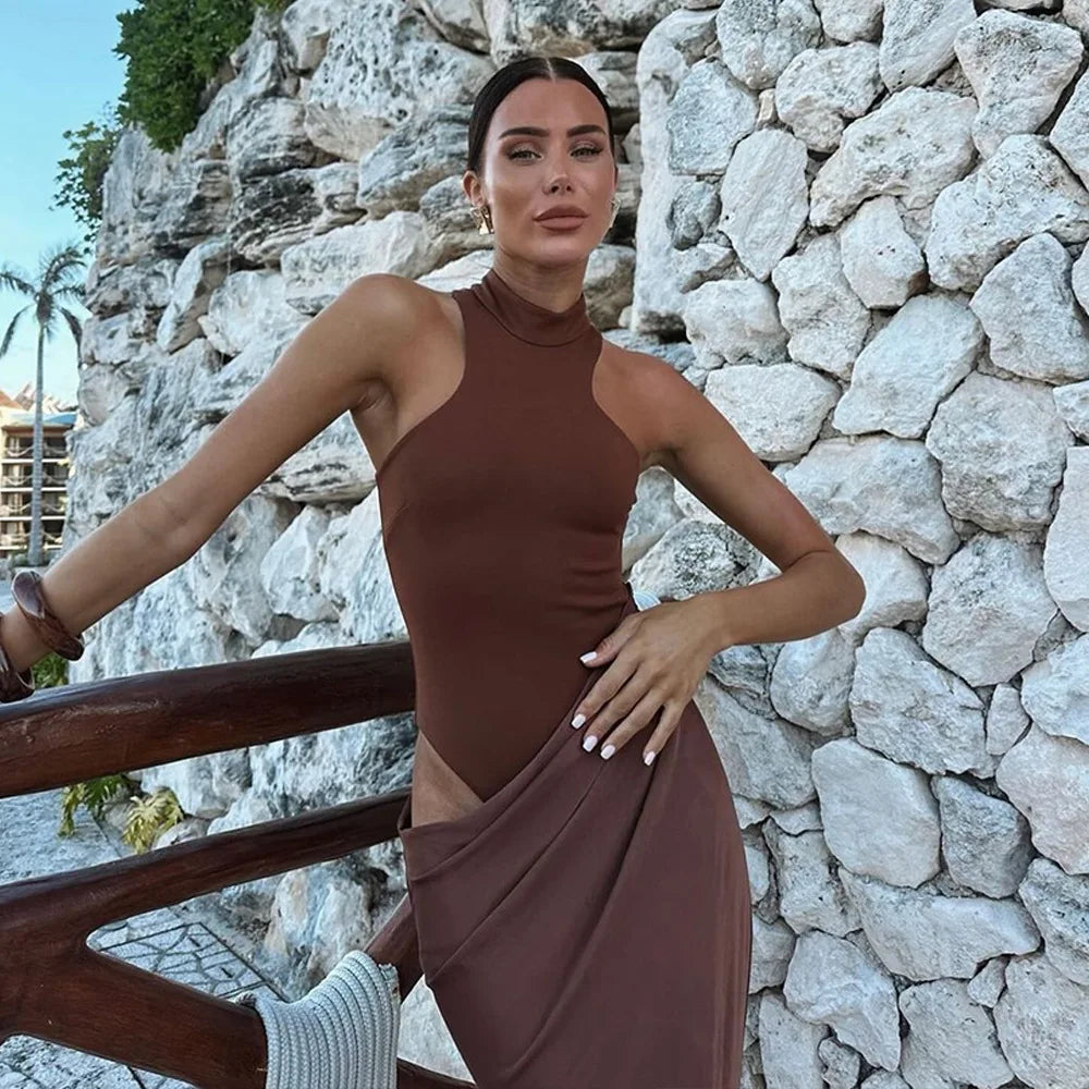 Woman in a brown dress standing against a stone wall.