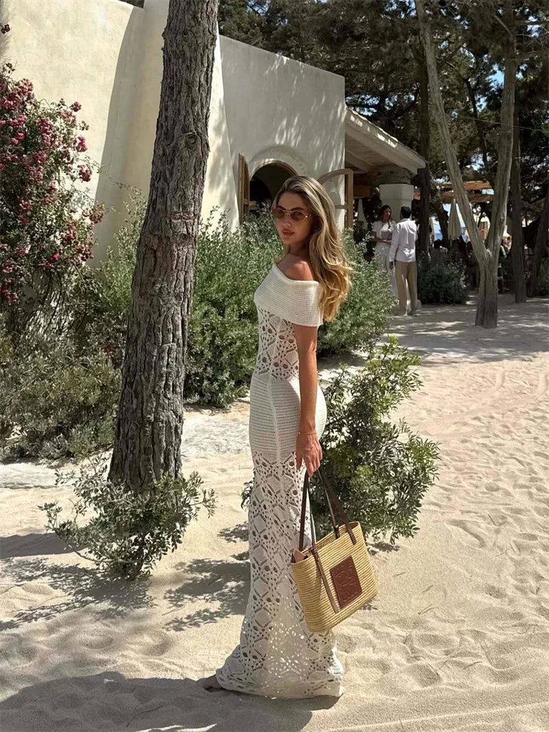 Woman in a white lace dress standing outdoors with a building and trees in the background