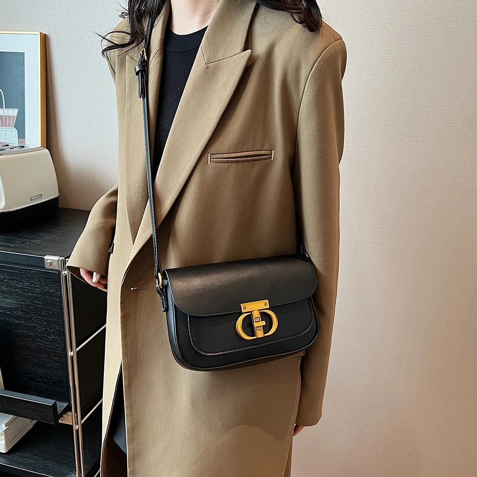 Person wearing a beige coat holding a black handbag with a gold clasp.