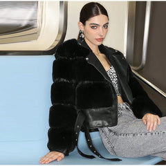 Woman wearing a black fur jacket and gray pants sitting on a blue seat.