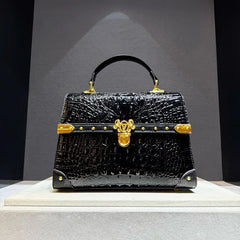 Structured crocodile embossed leather top handle bag in black with gold hardware.