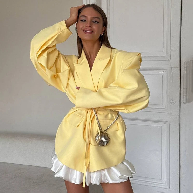 Woman wearing a yellow outfit with a white skirt, standing against a neutral background.