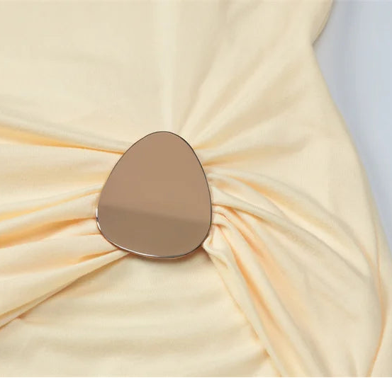 Close-up of a beige fabric with a metallic brooch on a light gray background