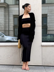 Woman in black outfit standing against a building with reflective windows.