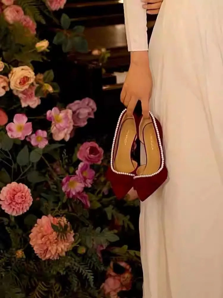 Red shoes with gold soles held by a person in front of floral decorations