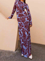 Woman wearing a long burgundy dress with blue leaf pattern against a beige wall.
