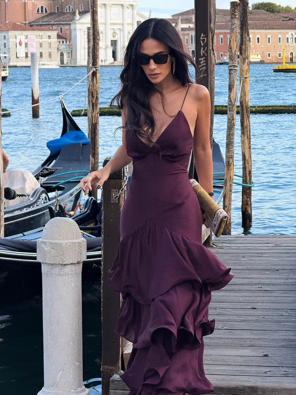 Woman in a purple dress standing by a dock with gondolas and buildings in the background.