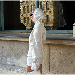 Person wearing a white outfit with a hood, standing in front of a stone building.