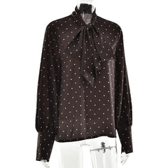 Black blouse with white polka dots and a tie neckline on a mannequin against a white background