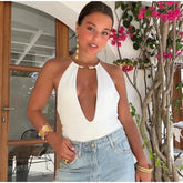 Woman wearing a white halter top and blue jeans standing in front of a floral plant.