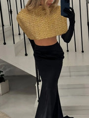 Person wearing a gold top and black skirt with gloves, standing on a staircase.