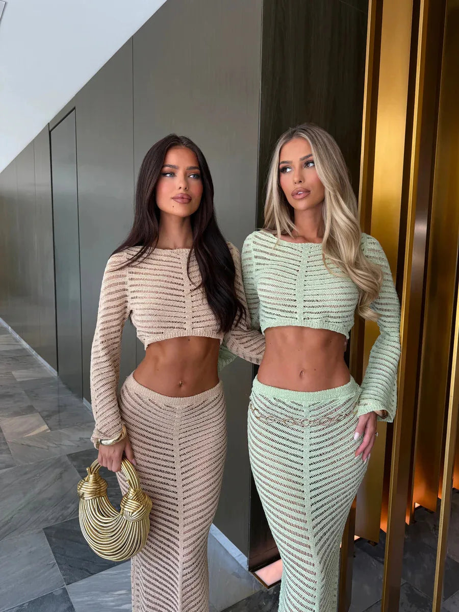 Two women in matching outfits standing indoors, one holding a gold handbag.