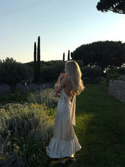 Woman in a white dress standing in a garden with trees and plants around.