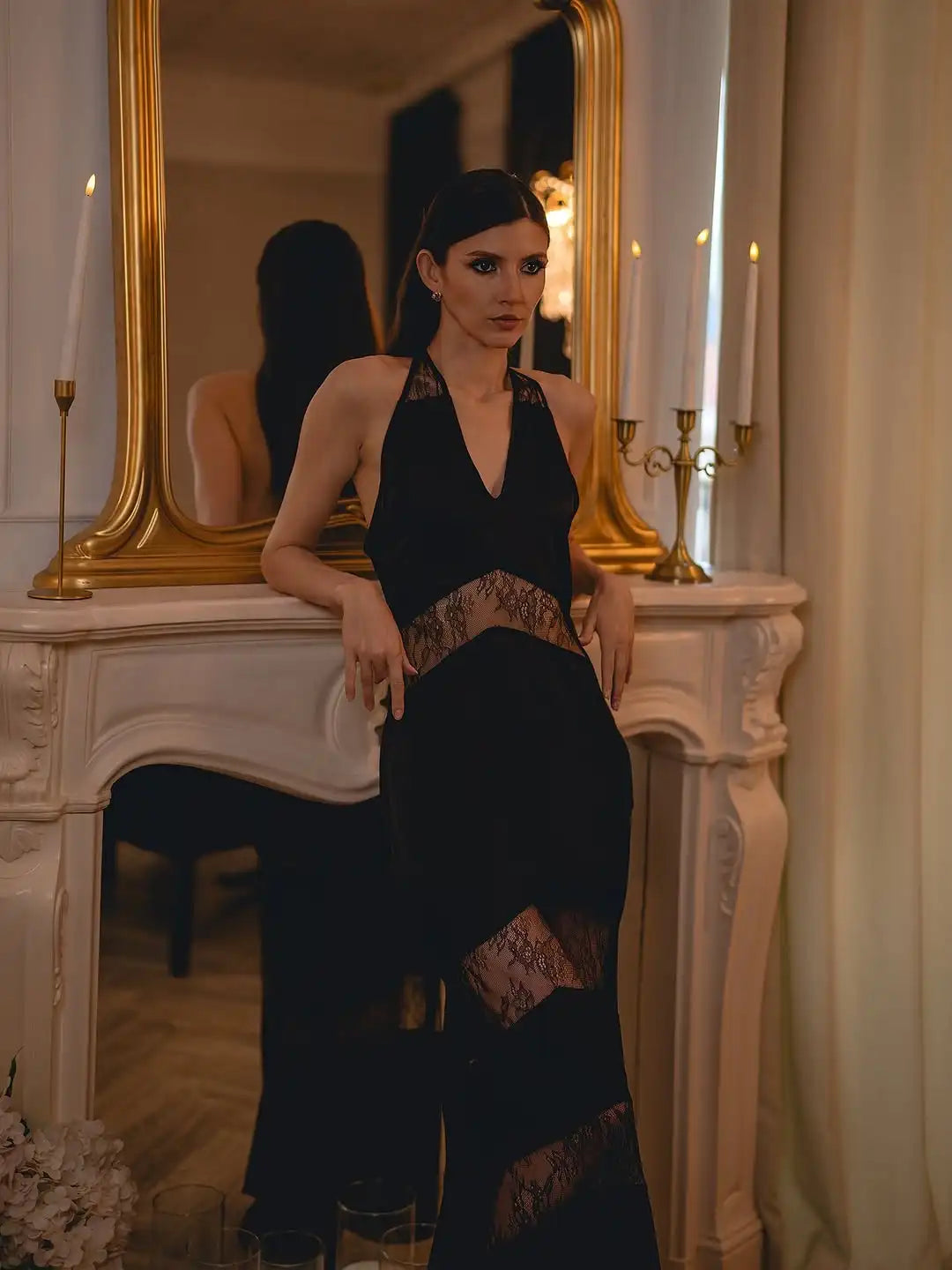 Woman in a black dress standing in front of a mirror in an elegant room.