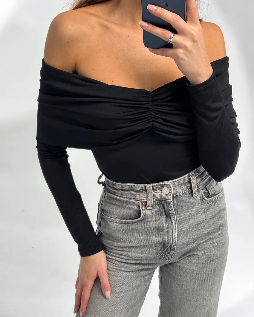 Person wearing a black off-shoulder top and gray jeans against a white background