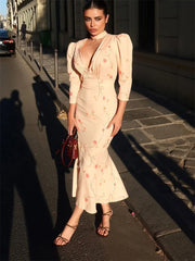 Woman in a light pink floral dress standing on a city street.