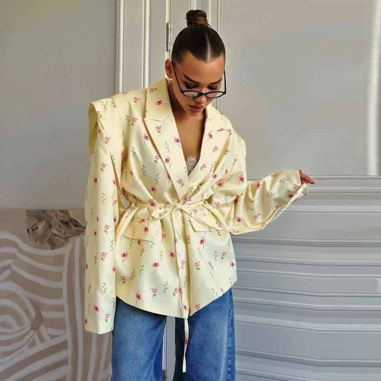 Woman wearing a light yellow floral blouse and blue jeans indoors.
