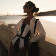 Model wearing a monochrome paneled swimsuit and white shirt at sunset