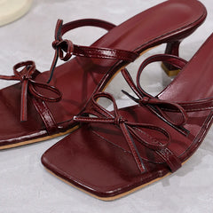 Pair of maroon high-heeled sandals with bow details on a light gray background