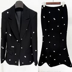 Black blazer and skirt with white embellishments on hangers against a white background