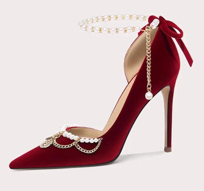 Red high-heeled shoe with gold chain and pearl decorations on a light gray background