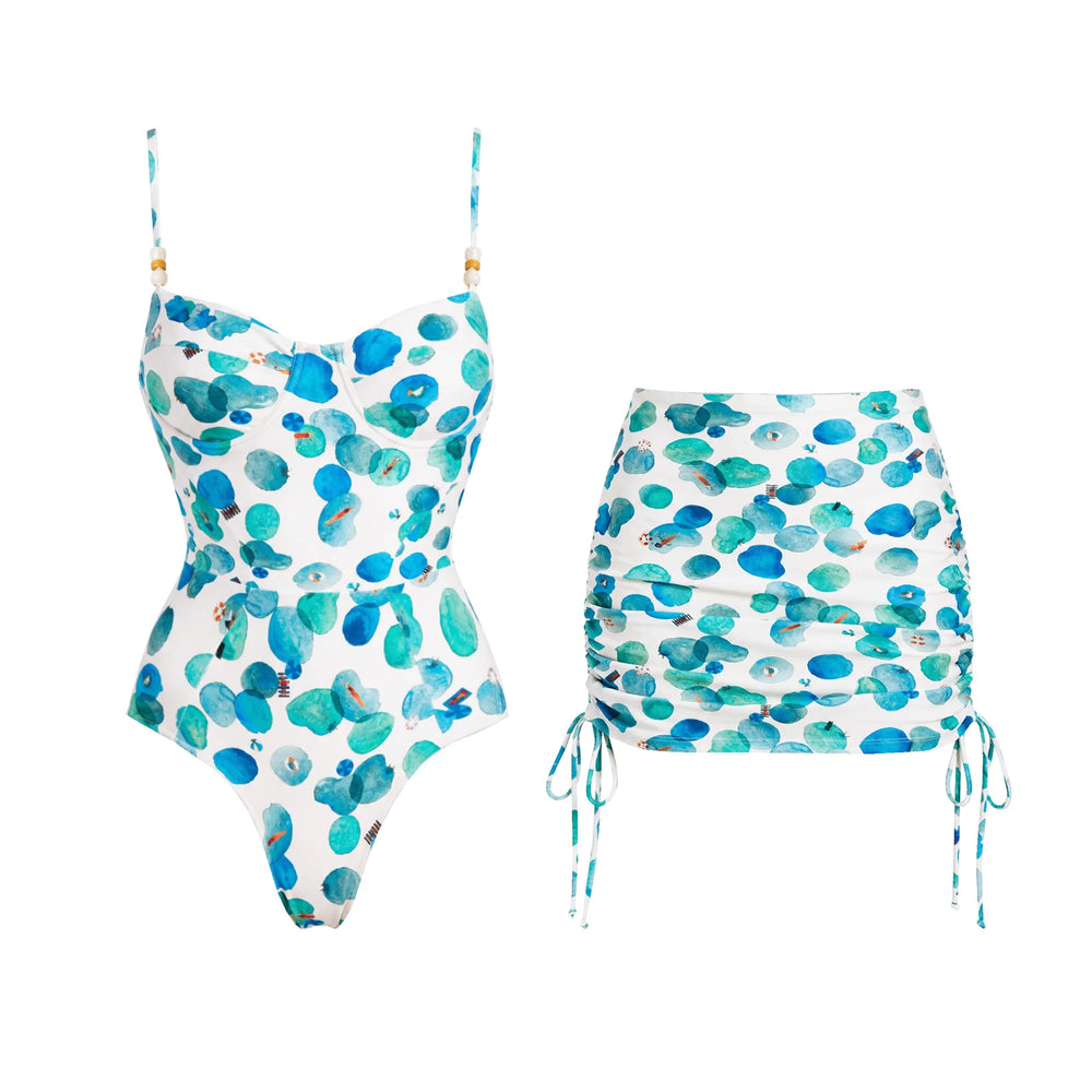 White one-piece swimsuit with abstract blue and green dots and a matching ruched skirt.