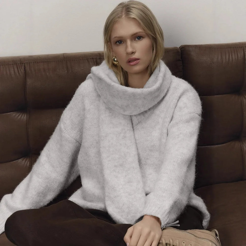 Woman wearing a light gray sweater sitting on a brown leather couch.