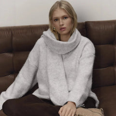 Woman wearing a light gray sweater sitting on a brown leather couch.