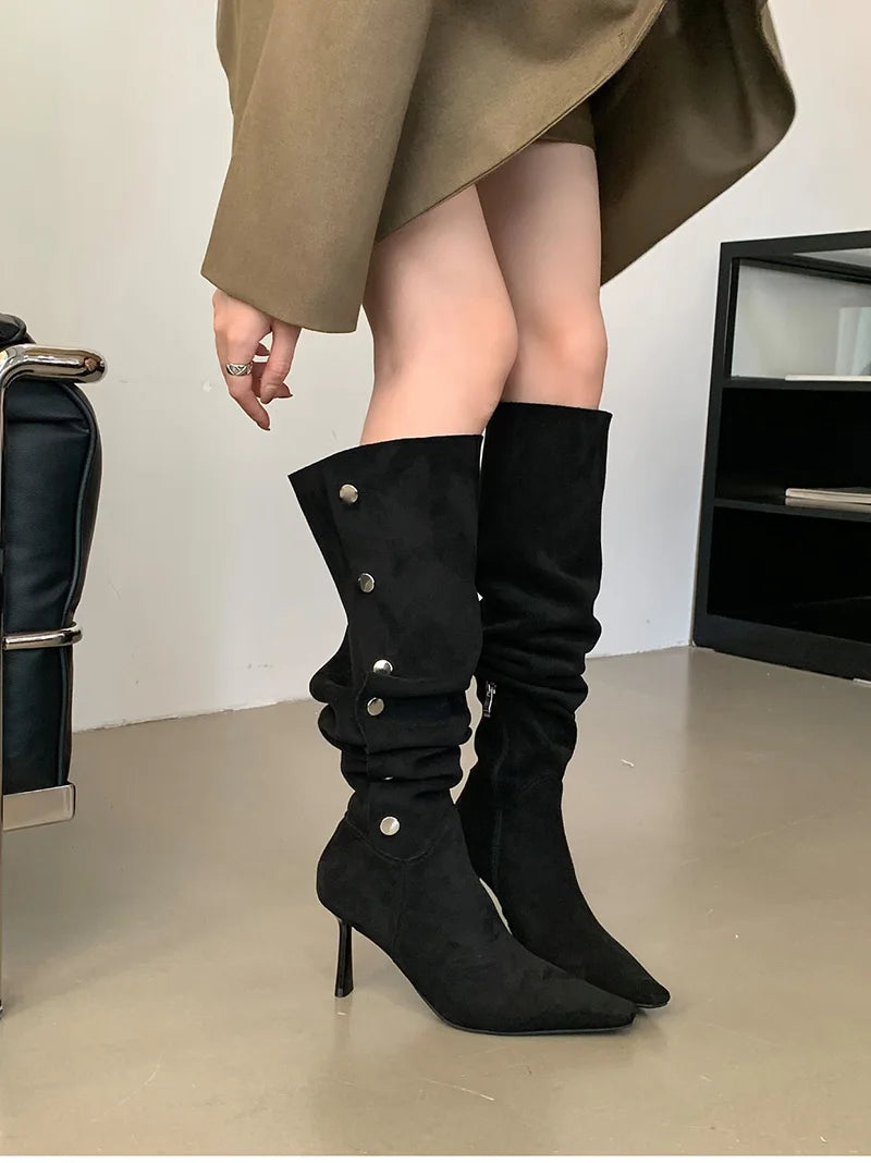 Black knee-high boots with high heels worn by a person in a neutral setting.