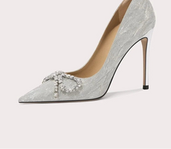 Silver high-heeled shoe with decorative element on a light gray background