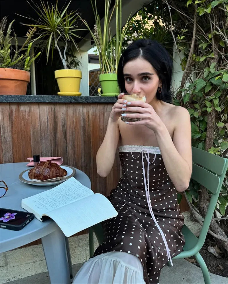 Woman sitting outdoors, drinking from a cup with plants and a table in the background