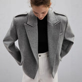 Person wearing a gray coat over a black top and white pants on a light gray background