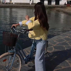 Woman in a yellow jacket standing next to a bicycle by a waterfront.