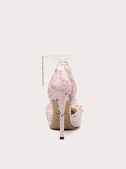 Floral high-heeled shoe with decorative chain on a light pink background
