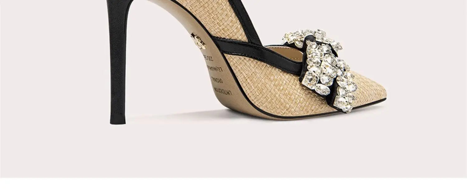 Beige high-heeled shoe with black strap and decorative embellishments on a light background