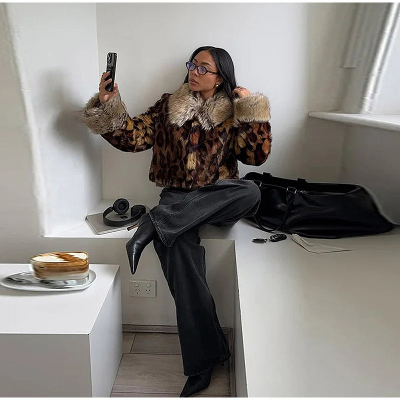 Person sitting on a white ledge wearing a patterned coat with fur trim, taking a selfie.