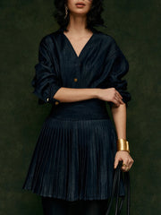 Woman wearing a dark blue pleated dress against a dark green background