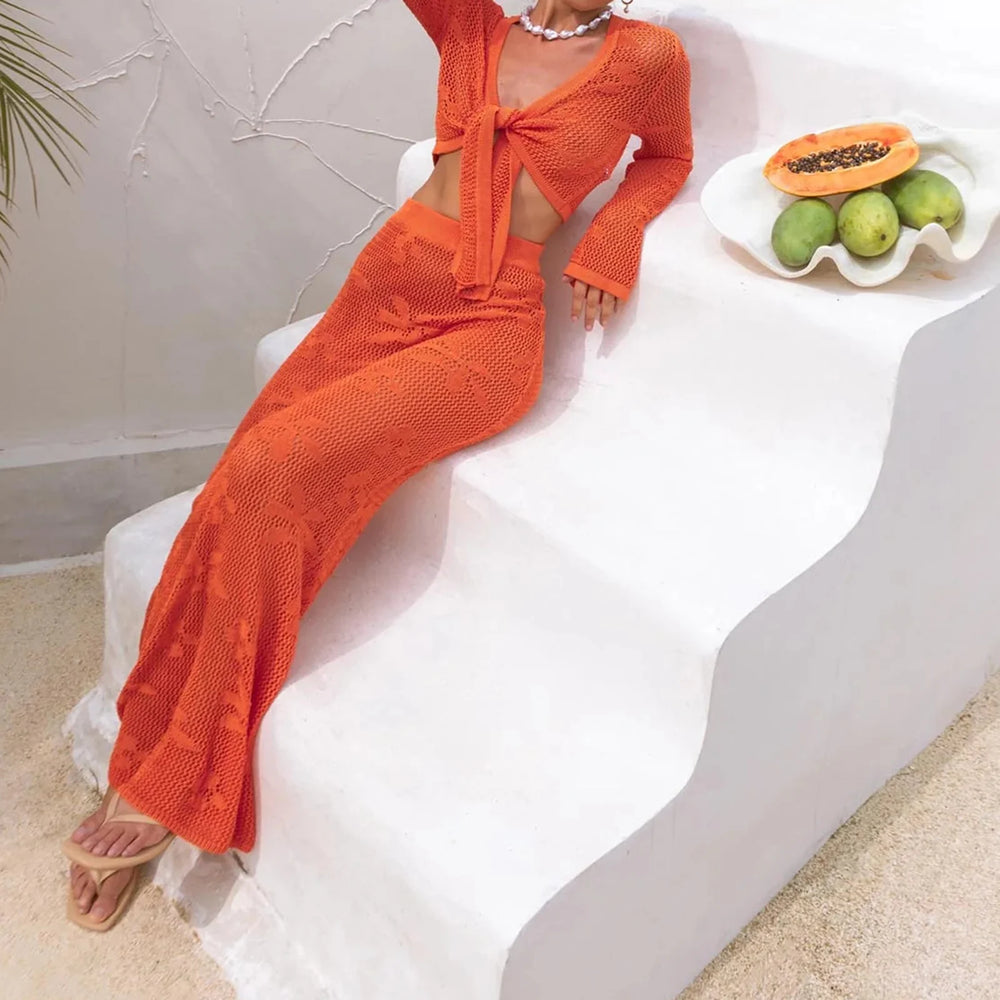 Person wearing an orange knit outfit sitting on a white chair with a bowl of fruit in the background.