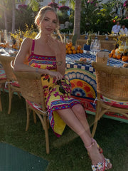 Woman in a colorful dress sitting at an outdoor event with tables and decorations.