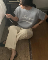 Person wearing a light blue sweater with text, sitting on a bed.