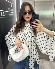 Woman taking a mirror selfie wearing a polka dot blouse and sunglasses, holding a phone.