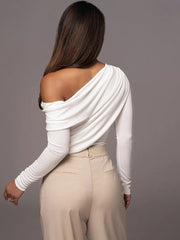 Woman wearing a white off-shoulder top and beige pants against a gray background