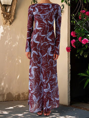 Person wearing a long burgundy dress with floral pattern against a beige wall and plant.