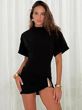 Woman wearing a black outfit with gold accessories against a white curtain background