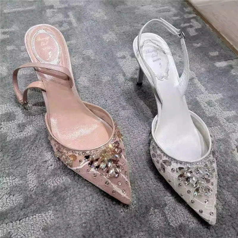 Pair of pink and white high-heeled shoes with embellishments on a textured surface